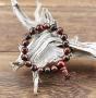 Ce bracelet-mala tout en raffinements est composé de perles de bois d'Abélia foncé. Il est accompagné d'un pendant de bois de Santal rouge incrusté à l'or biface du nom du Bouddha et orné de six perlettes du Grenat: un bel ensemble pour un bracelet-chapel