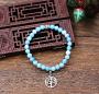 Délicat bracelet de perles Larimar d'un bleu tendre mais soutenu; une couleur recherchée pour son lien avec la symbolique de l'élévation et de protection. Orné de deux motifs de métal argenté dont une perle-cylindre Mantra traditionnelle dans le bouddhism